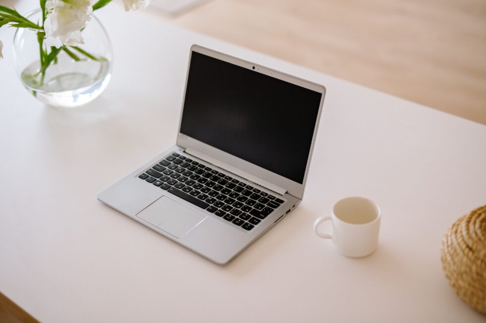 Laptop auf einem hellen Tisch mit Tasse und Blumen